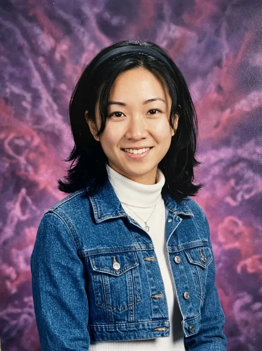 A 90s yearbook portrait of a woman with a headband in a cropped denim jacket and white turtleneck against a purple and pink backdrop