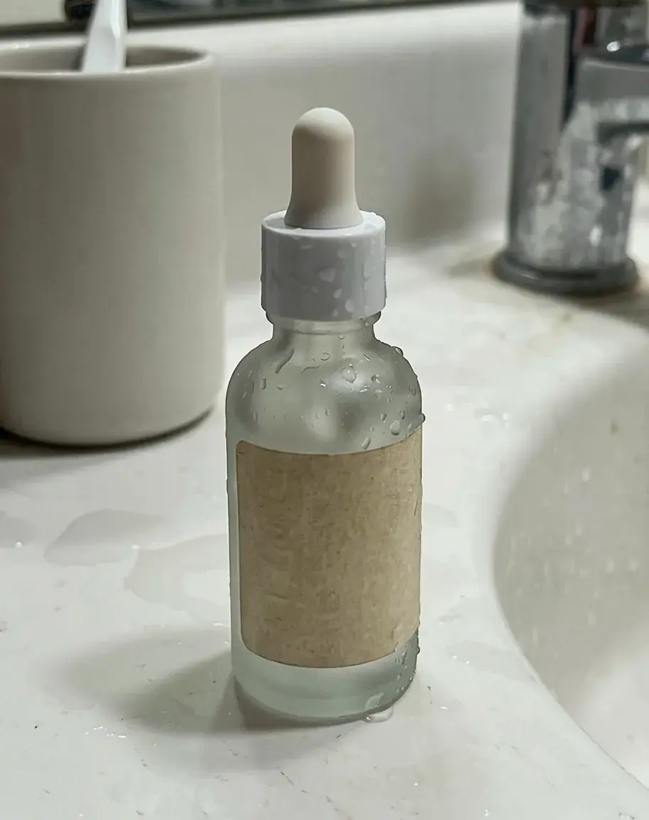 Flux 3 Image: the serum bottle still on the bathroom sink, a few drops on the glass, framed much like the phone photo