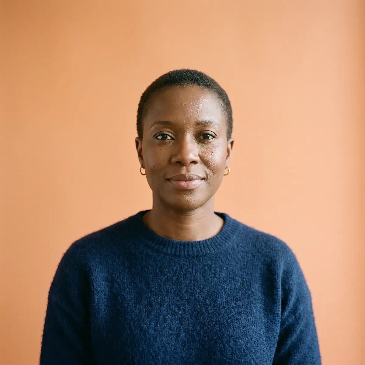 A woman with close-cropped hair, gold hoops and a textured navy knit, more headroom above her, made on Nano Banana 2.1