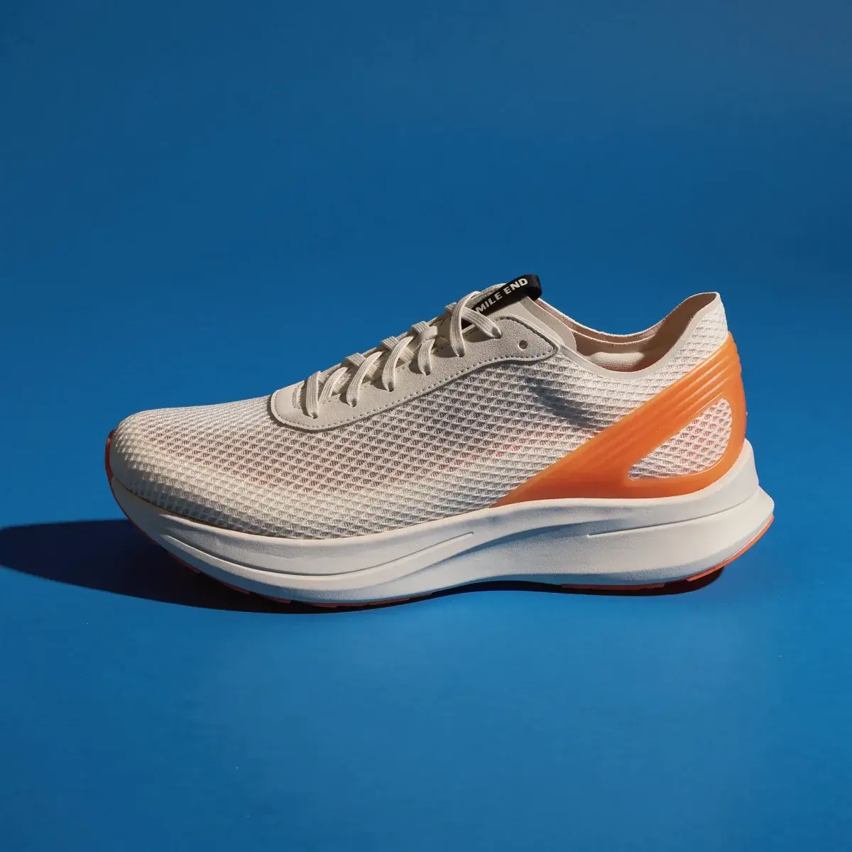 The shoe in profile on a seamless floor and wall in a teal-leaning blue, a dark shadow to the left