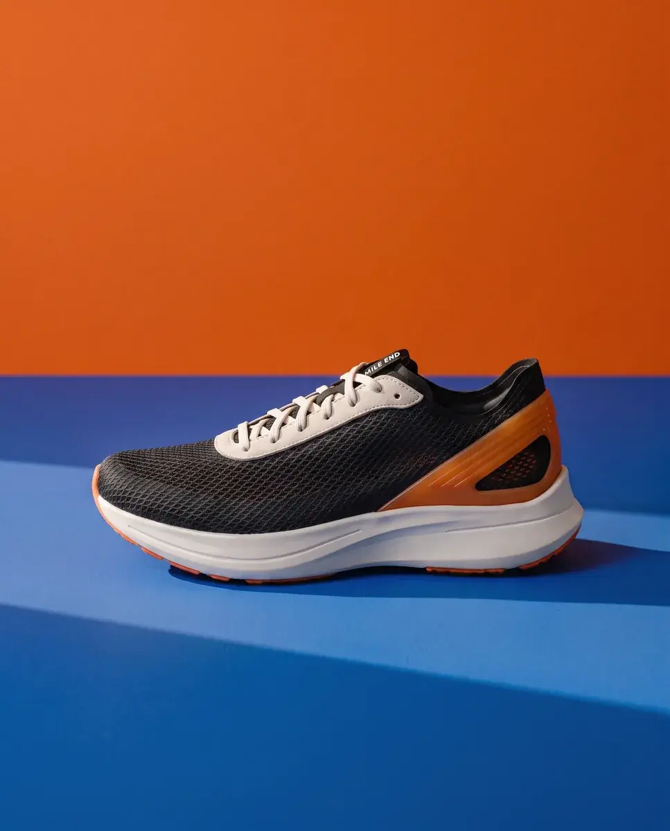 The color planes shot with the shoe's mesh upper turned black, the white laces, orange heel clip, cobalt floor and orange wall unchanged