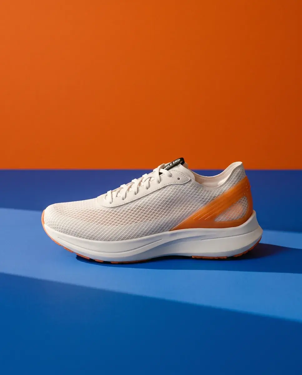 The shoe in side profile on a cobalt floor against a flat orange wall, hard sun across the blue