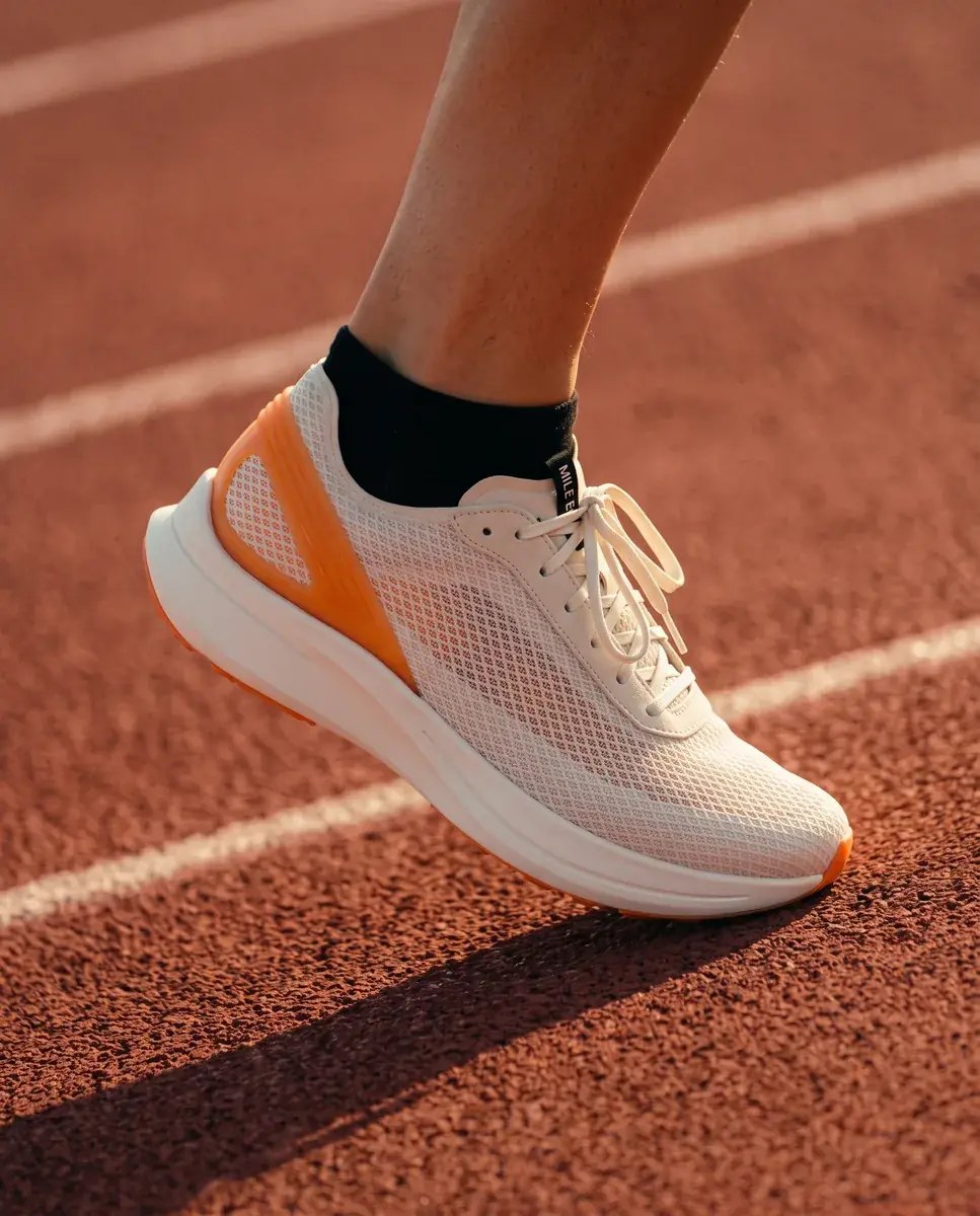 A runner's lower leg in a black sock mid-stride on a red track lane, the shoe's toe still touching, white lane lines behind