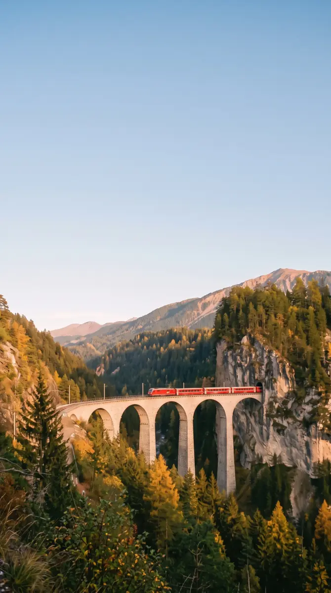 The viaduct recomposed by AI as a tall story frame: the top half clear evening sky, the curved stone viaduct and the small red train in the lower middle among golden larches