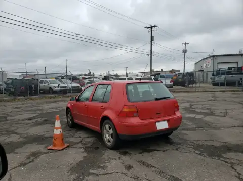 The same red hatchback after Ideogram Edit: the cars on both sides gone, empty asphalt around it, the hatchback, cone and fence unchanged